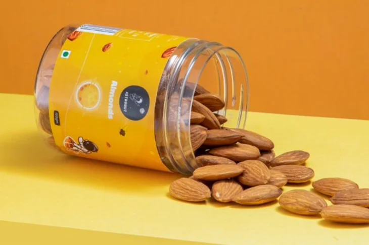 On a vibrant yellow background, almonds in a glass jar spilled on the table, symbolizing talented photography.