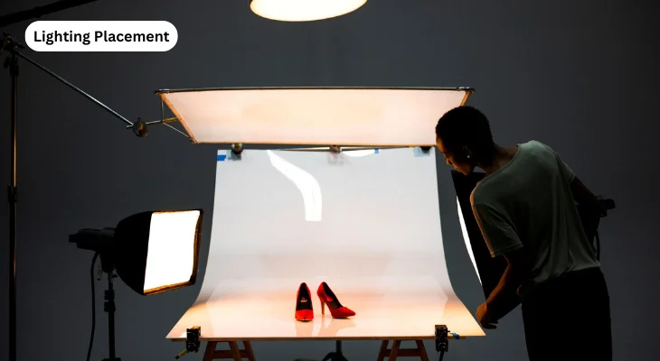 A man stands before a light box, showcasing a striking red shoe improved by strategic lighting.