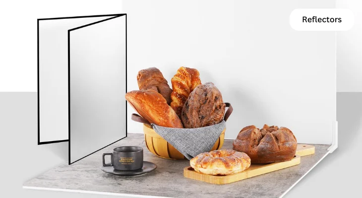 Bread in a basket and on a board, with a cup nearby, lit by reflectors against a white background.