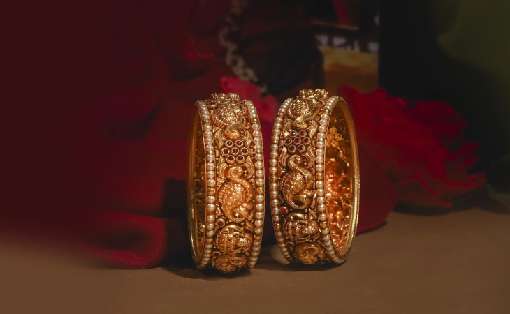 Ornate gold bangles adorned with intricate designs and pearls showcased in a stylish lifestyle photoshoot.
